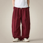 Kaio - Pantalón Urbano Wesley Unisex | Replace only the background of this product photo with a seamless warm greige studio backdrop — a soft neutral tone between light taupe and cream, with a subtle
