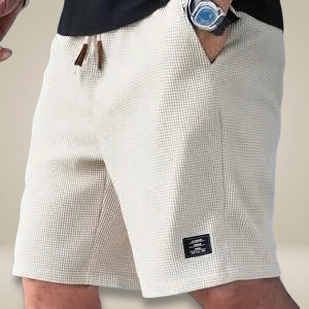 Short de Verano con cordón ajustable | Replace only the background of this product photo with a seamless warm greige studio backdrop — a soft neutral tone between light taupe and cream, with a subtle